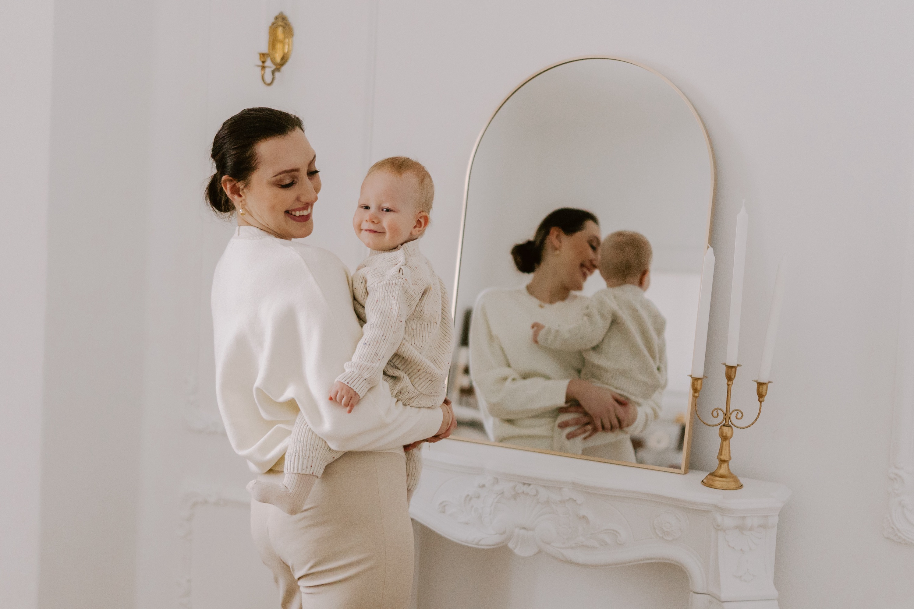Mama z dzieckiem na rękach odbijają się w lustrze nad kominkiem